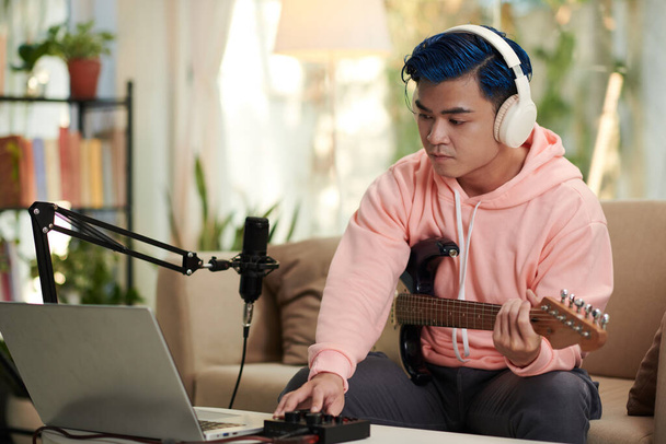 Luova nuori mies editointi melodia hän pelaa sähkökitara ja ladattu kannettavaan tietokoneeseen - Valokuva, kuva