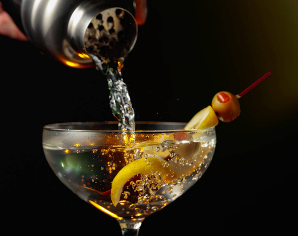 Martini con olive verdi e limone. Il cocktail viene versato da uno shaker in un bicchiere. - Foto, immagini