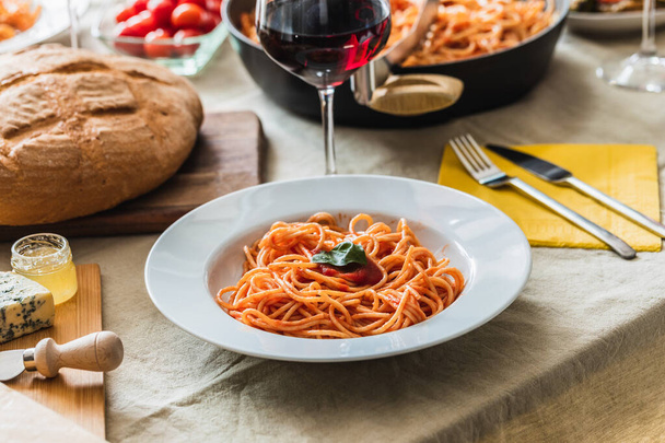 トマトソースのスパゲティプレートを中心にテーブルセッティング。背景に赤ワインのパン、カトラリー、ガラス - 写真・画像