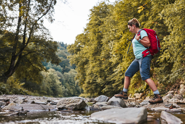 Traveling trekking with backpack concept image. Backpacker female in trekking boots crossing mountain river. Woman hiking in mountains during summer trip. Vacation trip close to nature. Natural scenery - Fotoğraf, Görsel