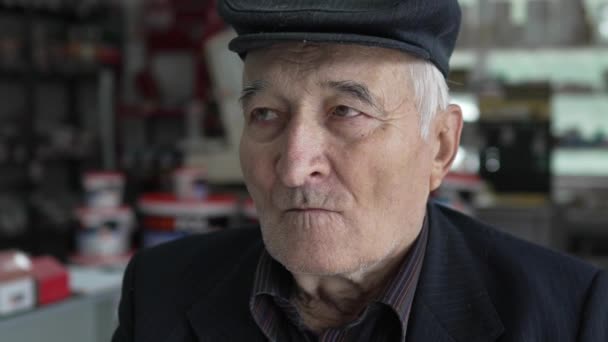 Porträt eines Mannes kaukasischen Rentner Großvater sitzen drinnen tragen Mütze Hut Blick in die Kamera bei Tag Zeitlupe Nahaufnahme - Filmmaterial, Video