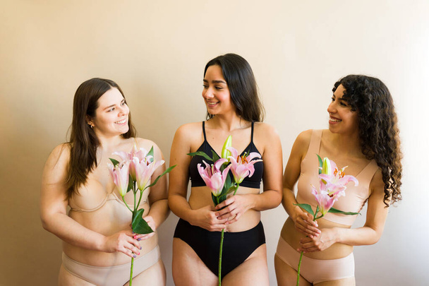 Happy diverse drei Frauen mit Blumen fühlen sich feminin und glücklich über Körpervielfalt und Selbstliebe - Foto, Bild