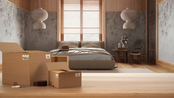 Wooden table, desk or shelf with stack of cardboard boxes over blurred view of japandi bedroom in minimal style, interior design, moving house concept with copy space - Fotó, kép