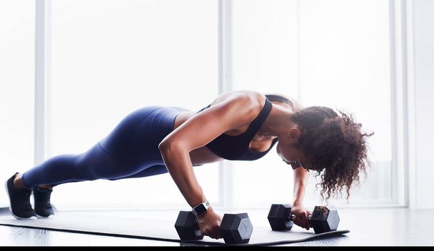 Starke Körper werden mit Disziplin gestaltet. eine junge Frau, die in einem Fitnessstudio mit Hanteln trainiert - Foto, Bild