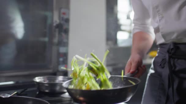 Gehakt schot van professionele mannelijke chef-kok gooien groenten op koekenpan tijdens het koken in restaurant keuken - Video