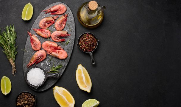 Boiled shrimp on a board, lemon slices, spices on a black background, top view. Copy space - Photo, Image