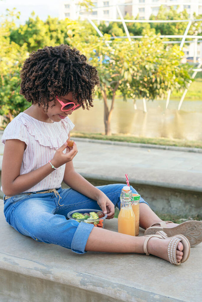 Ragazza ispanica mangiare verdure mentre seduto nel parco in estate - Foto, immagini