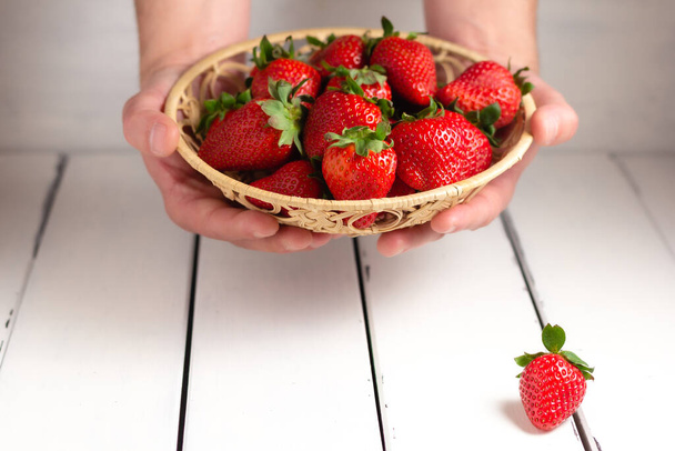 Hand holding a strawberry on a bascket on white wooden background. Close up. - Fotoğraf, Görsel