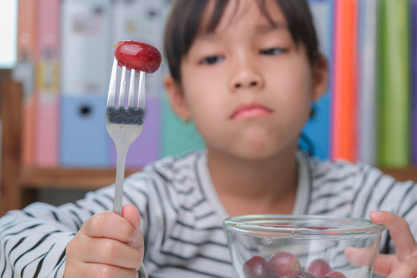 Children don't like to eat fruits. Cute young Asian girl refusing to eat healthy fruits. Nutrition and healthy eating habits for children. - Photo, Image