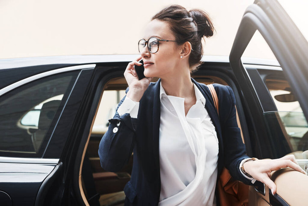 I have arrived. a confident young businesswoman getting out of a car while holding a cellphone outside during the day - Foto, Imagen