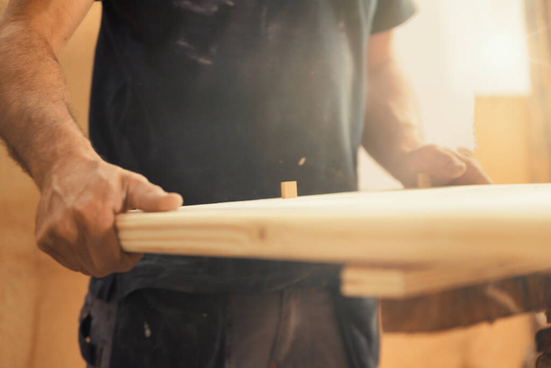 Starke Tischlerhände halten, führen, halten, schieben und bewegen Holz, während sie mit leistungsstarken Schneidemaschinen in seiner Werkstatt arbeiten. Image vermittelt Stärke, Geschick und Risikobereitschaft - Foto, Bild