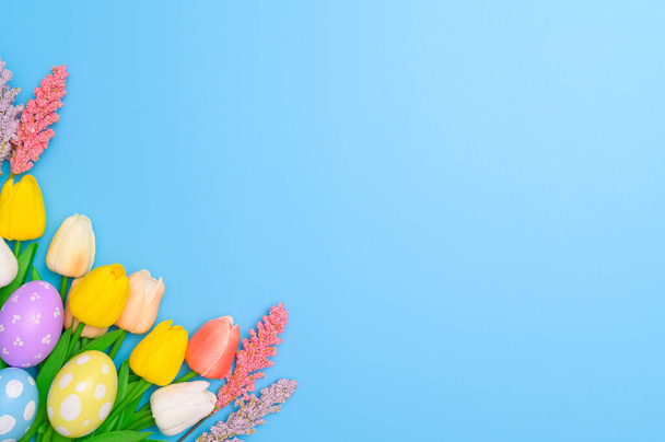 Frohe Osterfeiertage Grußkarte Konzept. Bunte Ostereier und Frühlingsblumen auf blauem Hintergrund. Draufsicht, flache Lage, Kopierraum. - Foto, Bild