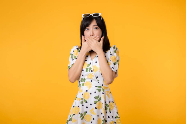 Портрет молодой азиатской женщины, которая молчит, делится секретом, делает табу жест носит случайное весеннее платье, изолированное на желтом фоне. Тихо, тихо. - Фото, изображение
