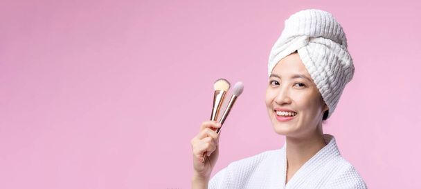 Retrato joven mujer asiática feliz con maquillaje natural cara celebración cosmética piel polvo colorete aislado sobre fondo rosa. Las hembras aplican tratamiento de cepillo para la piel. producto de belleza, concepto de cosmetología. - Foto, imagen