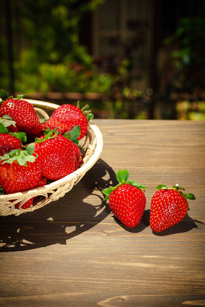 Berries of juicy strawberries in a wicker bowl on a white shabby wooden table in rustic style with copy space - Fotó, kép