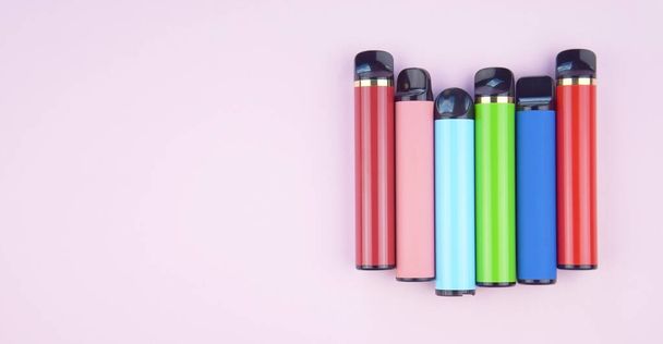 Σετ πολύχρωμων ηλεκτρονικών τσιγάρων μιας χρήσης σε ροζ φόντο. Η έννοια του σύγχρονου καπνίσματος, ατμίσματος και νικοτίνης. - Φωτογραφία, εικόνα
