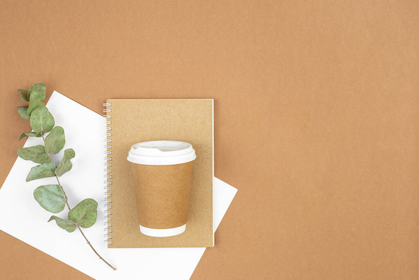 Craft paper coffee cup, notebook and eucalyptus sprig on eco background, flat lay, copy space, eco and paper recycling concept. - Fotografie, Obrázek