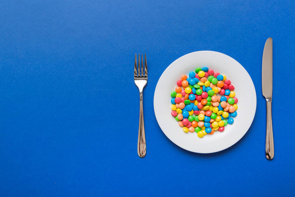 cutlery on table and sweet plate of candy. Health and obesity concept, top view on colored background. - Foto, Imagem