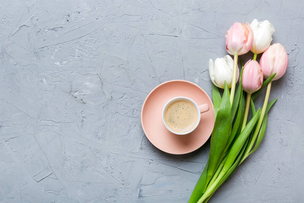 Spring background with flowers, a cup of coffee and a bouquet of pink and white tulips on colored table background with place for text. Copy space top view. - Фото, изображение