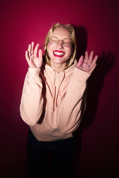 A cheerful young blond woman dancing in studio isolated on magenta background. Viva magenta, color of the year. - Photo, Image