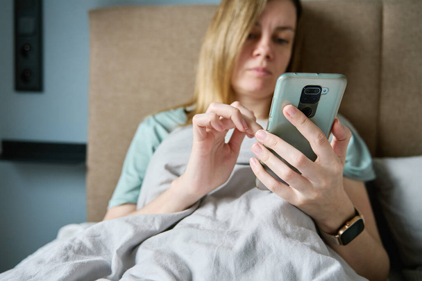 Γυναίκα ψύξη στο κρεβάτι το πρωί και να χρησιμοποιήσετε smartphone, τεμπέλης πρωί - Φωτογραφία, εικόνα
