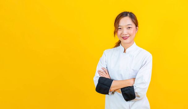 Portrait studio shot of asian woman chef with professional uniform posing with cross hand in confident isolated on yellow background for culinary and restaurant concept - Foto, immagini