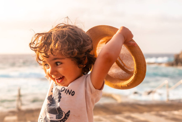 Portrait of boy in hat smiling at summer sunset on the beach, summer vacation - Фото, зображення