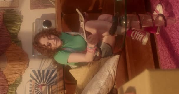 Κάθετη του τζίντζερ Καυκάσιος κορίτσι κάθεται στον καναπέ στο σαλόνι στη δεκαετία του ογδόντα αισθητική, μιλώντας σε ρετρό τηλέφωνο, χαμογελώντας - Πλάνα, βίντεο