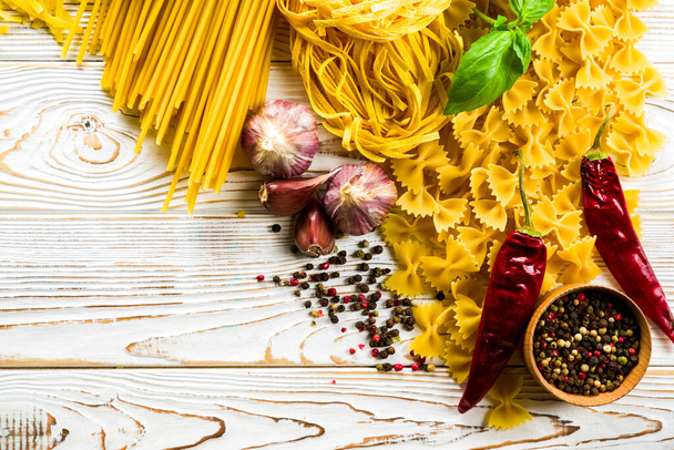 Сырая макароны и спагетти с помидорами черри и травами и специями на светлом столе, взятые с высокого угла - Фото, изображение