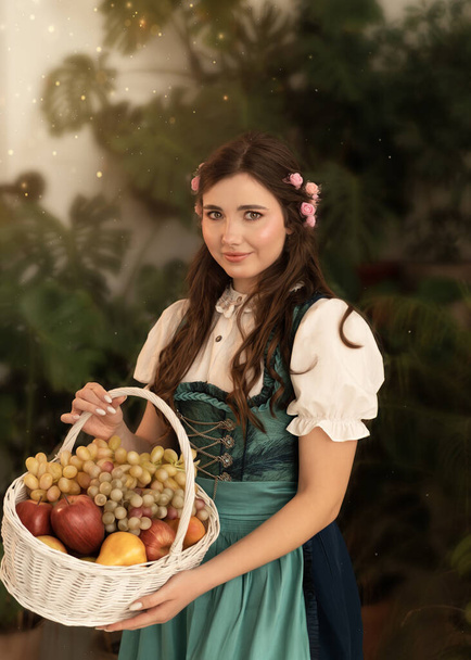 A young girl with a basket of fruit standing in a garden dressed in a 19th century bavarian dress. - Foto, afbeelding
