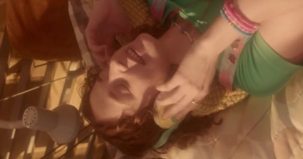 Verticale di zenzero ragazza caucasica in retro cuffie over-ear, ascoltare musica, sdraiato sul divano a casa - Filmati, video