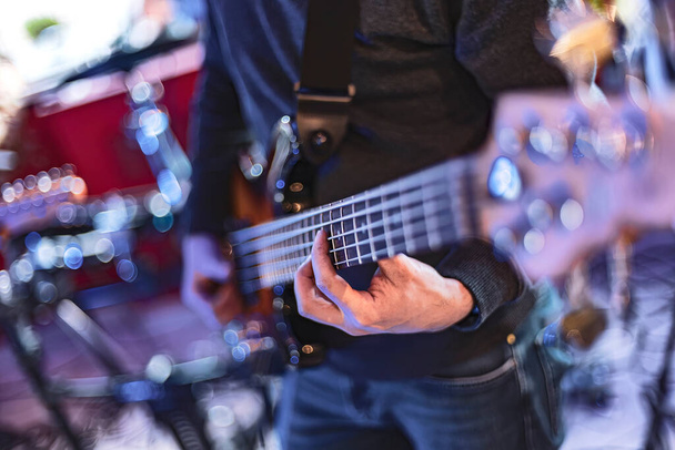 Close-up detail of a bassist's hand playing the frets of a bass guitar during a live performance. - Foto, Imagen