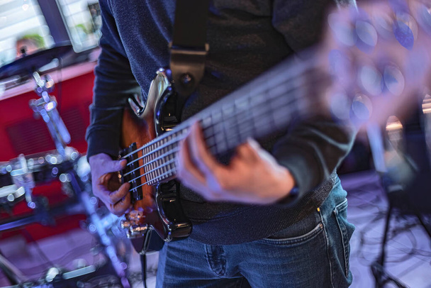 Close-up detail of a bassist's hand playing the frets of a bass guitar during a live performance. - Photo, Image