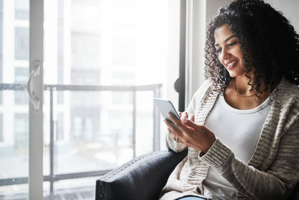 Mal sehen, was in den sozialen Medien los ist. eine fröhliche junge Frau entspannt sich, während sie tagsüber mit ihrem Handy zu Hause SMS schreibt - Foto, Bild