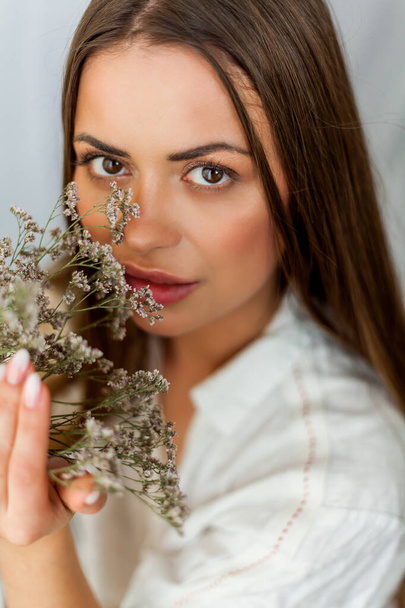 Portrait of beautiful young woman with long hair on white background with dried flowers. - Foto, afbeelding