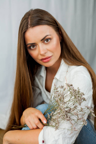 Portrét krásné mladé ženy s dlouhými vlasy na bílém pozadí se sušenými květy. - Fotografie, Obrázek