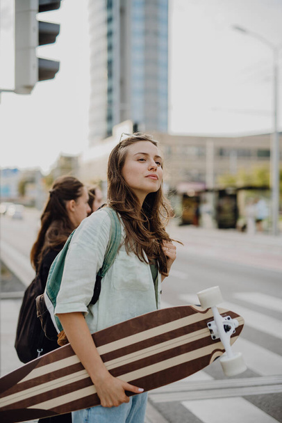 Young woman walking in city with a skateboard. Youth culture and commuting concept. - Foto, Imagen