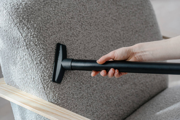 Woman vacuums modern armchair with soft upholstery, closeup view. Deep house cleaning of renovated furniture textile with hot steam and detergent. Housework and housekeeping concept - 写真・画像