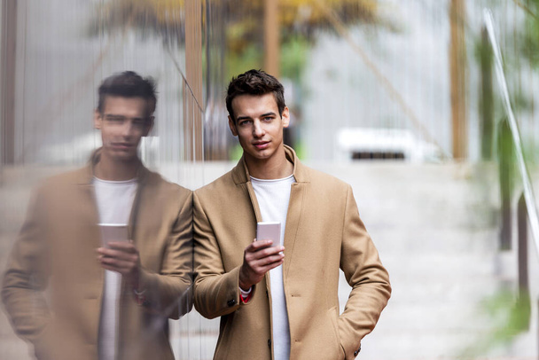 Portrait of stylish young man with coat standing outdoors and leaning on wall. - Foto, immagini