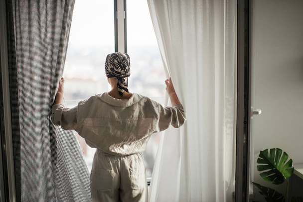 Rear view of young unhappy woman with cancer standing in front of the window. - Foto, immagini