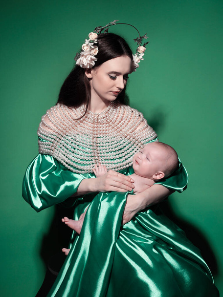 A young, modern, beautiful loving mommy holds hands, kisses her adorable baby in a bodysuit, expresses affection, feels love, close-up. Happy mother's day, motherhood, carefree childhood, guardianship concept - Photo, image