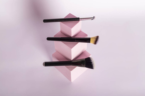 Set of makeup brushes arranged on pink cubic stands - Фото, изображение