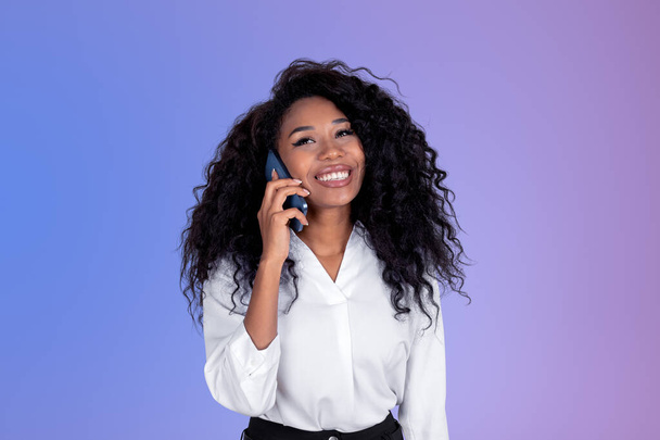 Smiling black businesswoman talking on the phone, african woman portrait on purple gradient background. Concept of communication and social media - Фото, изображение