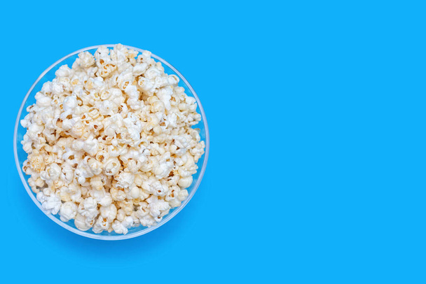 Popcorn in a large glass bowl on a blue background with a top view. Crispy classic popcorn snack for watching movies and series. Delicious light snack for watching TV. Free space for text - Фото, зображення