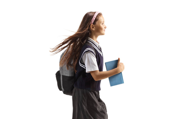 Profile shot of a schoolgirl with long hair carrying a book and running isolated on white background - Foto, Imagem