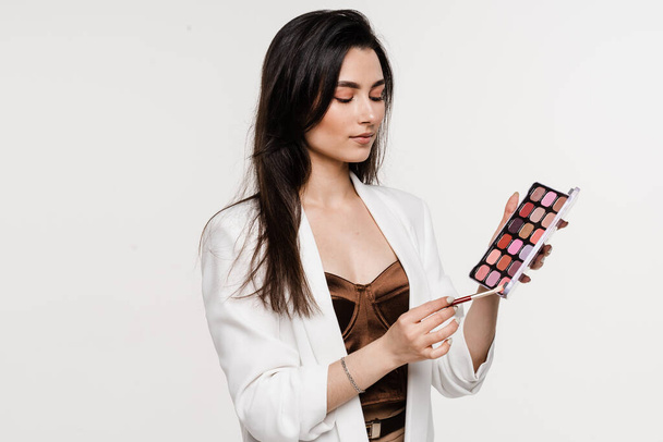 Девушка держит цветную палитру и кисть для макияжа в руках. Профессиональная косметика для визажиста для идеальной кожи - Фото, изображение