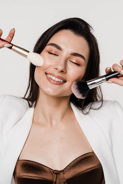 Professional make-up artist with makeup brushes on white background. Attractive girl is holding eye shadow brushes and smiling - Фото, зображення