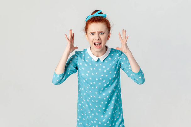 Portrait of angry depressed ginger woman arguing with her husband, screaming with hate and anger, being aggressive, wearing blue dress. Indoor studio shot isolated on gray background. - Photo, Image