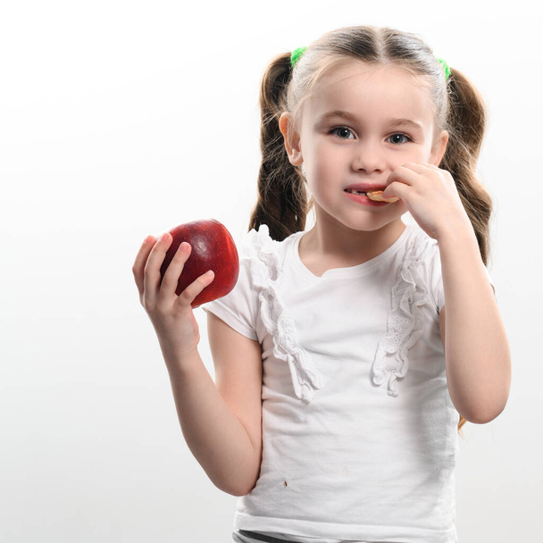 Egy kislány egy almát és chipset tart fehér alapon, az egészséges és egészségtelen ételválasztás koncepciója egy gyermek életében.. - Fotó, kép