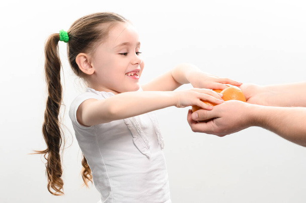 A little girl is given tangerines on a white background, a child takes tangerines, white background and copy space. - Foto, Imagen